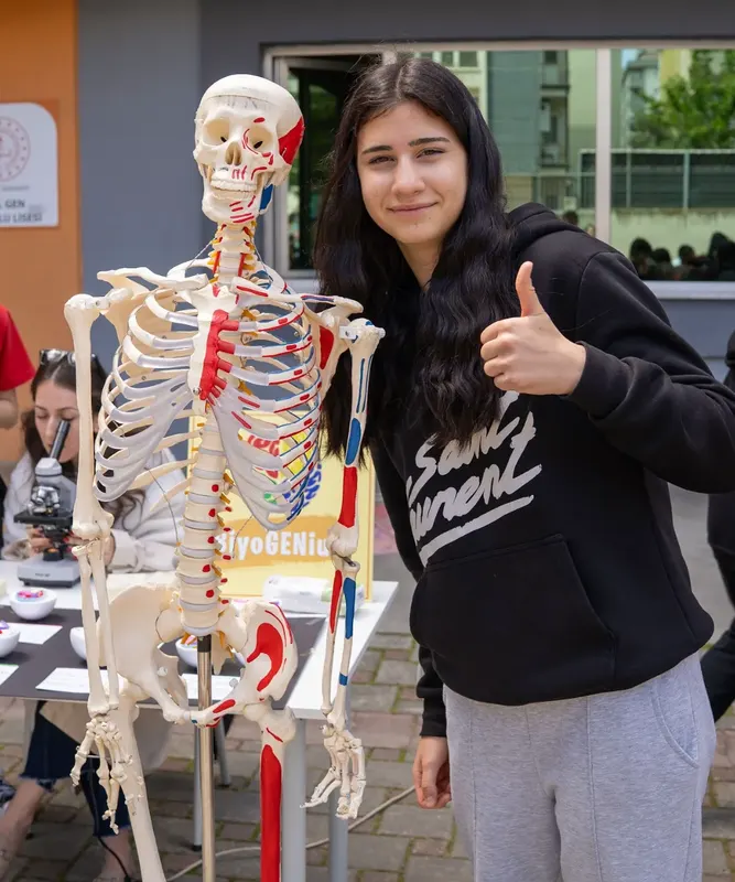 İskelet maketi yanında gülümseyen öğrenci